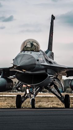 a fighter jet sitting on top of an airport tarmac next to a field with grass