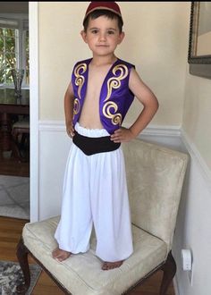 a young boy wearing a purple and gold costume standing on a chair in a living room