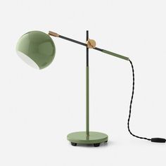 a green table lamp with a black cord attached to the base and a white wall behind it