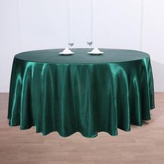 two wine glasses sitting on top of a green table cloth with white plates in front of it