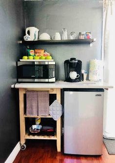 a small kitchen with stainless steel appliances and wood flooring, along with open shelving on the wall