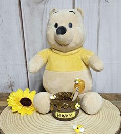 a teddy bear sitting on top of a table next to a sunflower and honey jar