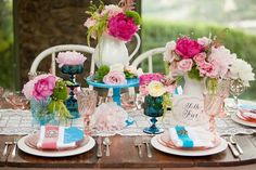 the table is set with pink and blue flowers in vases, plates, and napkins