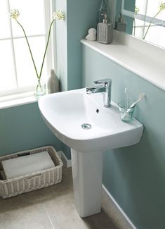 a bathroom sink sitting under a window next to a basket filled with toothbrushes