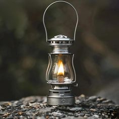 a small metal lantern with a lit candle in it on some rocks and trees behind it