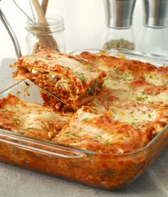 a glass casserole dish filled with lasagna sauce and cheese being lifted from the casserole