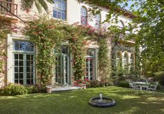 a large white house with lots of windows and flowers on the front wall, surrounded by lush green grass