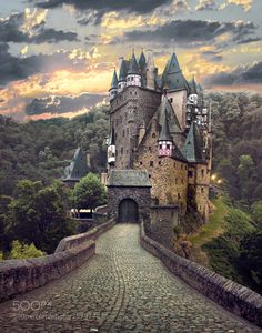 an old castle on top of a hill in the middle of a forest at sunset