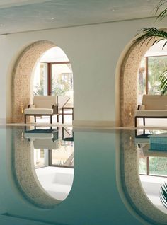 an indoor swimming pool with lounge chairs and potted palm tree in the background,