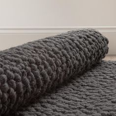 a large gray blanket laying on top of a wooden floor next to a white wall