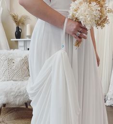 a woman wearing a white dress holding a bouquet of flowers in her right hand while standing next to a couch