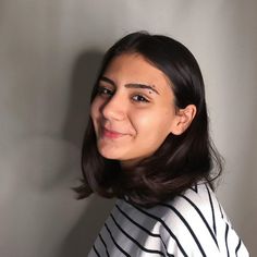 a woman with black and white stripes on her shirt smiling at the camera while standing against a gray wall