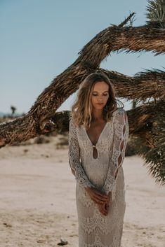 a woman standing in front of a palm tree wearing a long white dress and sandals