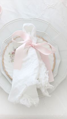 a white plate topped with a pink bow next to a tea cup and saucer