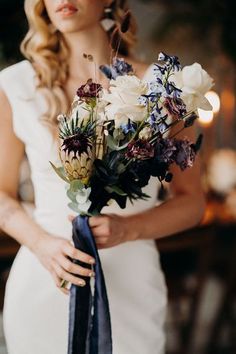 a woman holding a bouquet of flowers in her hands and wearing a white dress with blue sash