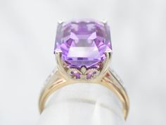 This stunning vintage amethyst ring has a pretty medium-hued purple amethyst in the center, that really flashes and flickers with vibrant violet reflections! Set into a lovely retro era mounting with structurally designed diamond shoulders and simple corner prongs, this vintage ring is a beautiful addition to anyone’s collection!Metal: 14K Yellow and White GoldGem: Amethyst 9.81 CaratsGem Measurements: 15.3 x 11.2 mm, Emerald CutAccents: 6 Diamonds totaling .06 Carats, SI2 in Clarity, K in ColorRing Size: 5.75Marks: “14K” Stamped on the inside band Vintage Amethyst Ring, Channel Set Diamond Band, Amethyst Ring Vintage, Retro Era, Amethyst And Diamond Ring, Engagement Ring Diamond Cut, Tanzanite Ring, Diamond Cocktail Rings, Diamonds And Gold