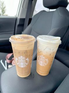 two cups of iced coffee sitting on the back seat of a car in front of someone