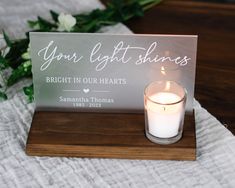 a lit candle sits next to a sign that says, your light shines bright in our hearts