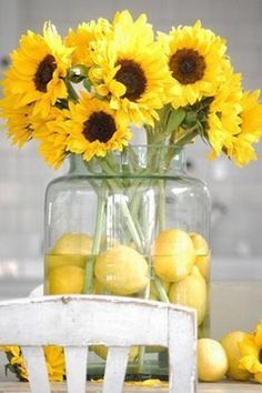 sunflowers and lemons in a glass vase on a table with an old chair