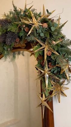 a christmas wreath with pine cones and greenery hanging on a mirror frame in a room