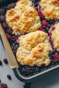 blueberry cobbler in a baking pan with fresh berries on the side and a wooden spoon