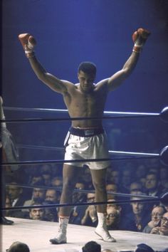 a man standing on top of a wrestling ring holding his hands up in the air