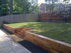 a wooden garden bench sitting in the middle of a lush green yard next to a fence