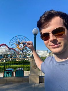 a man in sunglasses holding up a white ball with a ferris wheel in the background