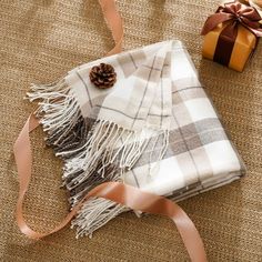 a blanket with a pine cone on it next to a wrapped present box and ribbon