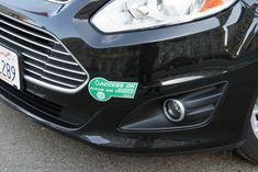 the front end of a black car with a green sticker on it's bumper