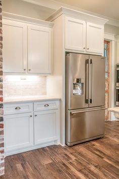 a stainless steel refrigerator in a kitchen with white cabinets and wood flooring on the walls