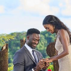 a man and woman standing next to each other in front of some trees holding hands