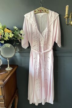 This unique set, designed in the 1970s, features a silk robe and nightgown that beautifully combine nostalgia and elegance, with floral embroidery adorning the necklines. Crafted from pure Rose silk, this magnificent set offers a luxurious and comfortable experience. The robe is adorned with delicate embroidery on the neckline, cuff edges, and pocket edges, while the nightgown's neckline reflects the same elegance with matching embroidery. Please check your measurements below. Size: Small Robe: Feminine V-neck Robe For Sleep, V-neck Lace Trim Robe For Daywear, Vintage V-neck Wedding Sleepwear, Pink Spring Robe For Bedtime, Pink Summer Robe For Bedtime, Summer Pink Robe For Bedtime, Pink Feminine Summer Robe, V-neck Robe With Lace Trim For Daywear, Lace Trim V-neck Robe For Daywear