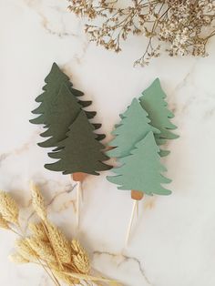 three wooden trees sitting on top of a white counter next to some dried grass and flowers