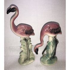 two pink flamingos sitting on top of each other in front of a white wall