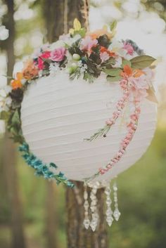 a white paper lantern hanging from a tree with flowers and leaves on it's side