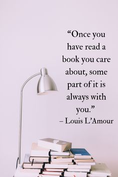 a stack of books sitting on top of a table next to a lamp and quote