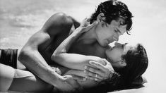 a man and woman laying on top of each other in the water together, kissing