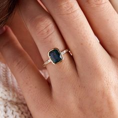 a woman's hand wearing a gold ring with a blue stone in the middle