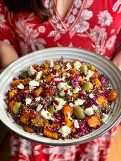 a woman holding a platter full of food with feta cheese and olives