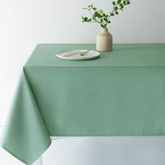 a green table cloth with a white plate and plant in a vase on the top