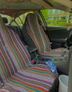 the interior of a car with two seats covered in multicolored blankets and an umbrella