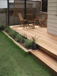 a wooden deck in the middle of a yard with lawn chairs and plants on it