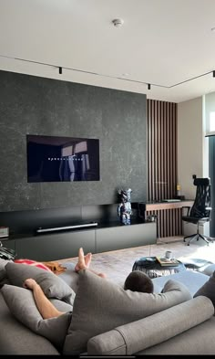 a person sitting on a couch watching tv in a living room with grey walls and flooring