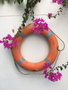 an orange life preserver with purple flowers hanging on the side of a white wall