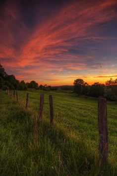 the sun is setting over a field with fence posts and trees in the foreground