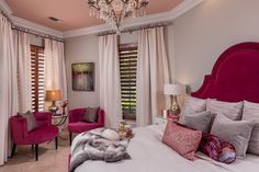 a bedroom with pink furniture and chandelier hanging from the ceiling in front of two windows