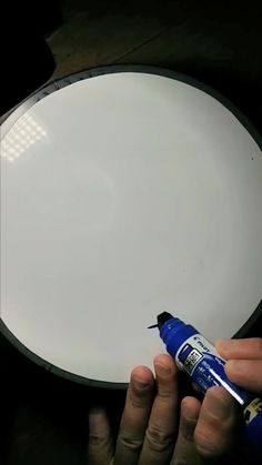 a person is painting a white plate with blue spray paint on the rim and it's surface