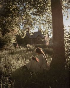 a woman sitting in the grass under a tree with her back to the camera,