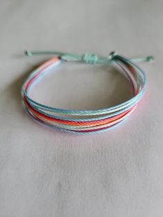 Adjustable multi-strand bracelet with a sliding square knot. Pink, neon orange, light blue, and blue strings. Multicolor Multi-strand Friendship Bracelets For Beach, Adjustable Multi-strand Bracelets For Summer, Blue Nylon Cord Friendship Bracelets With Sliding Knot, Blue Sliding Knot Friendship Bracelets In Nylon Cord, Blue Nylon Cord Friendship Bracelets For Beach, Blue Sliding Knot Friendship Bracelet With Nylon Cord, Blue Braided Bracelet With Sliding Knot For Summer, Trendy Blue Braided Bracelet With Sliding Knot, Blue Adjustable Cord Friendship Bracelets For Summer